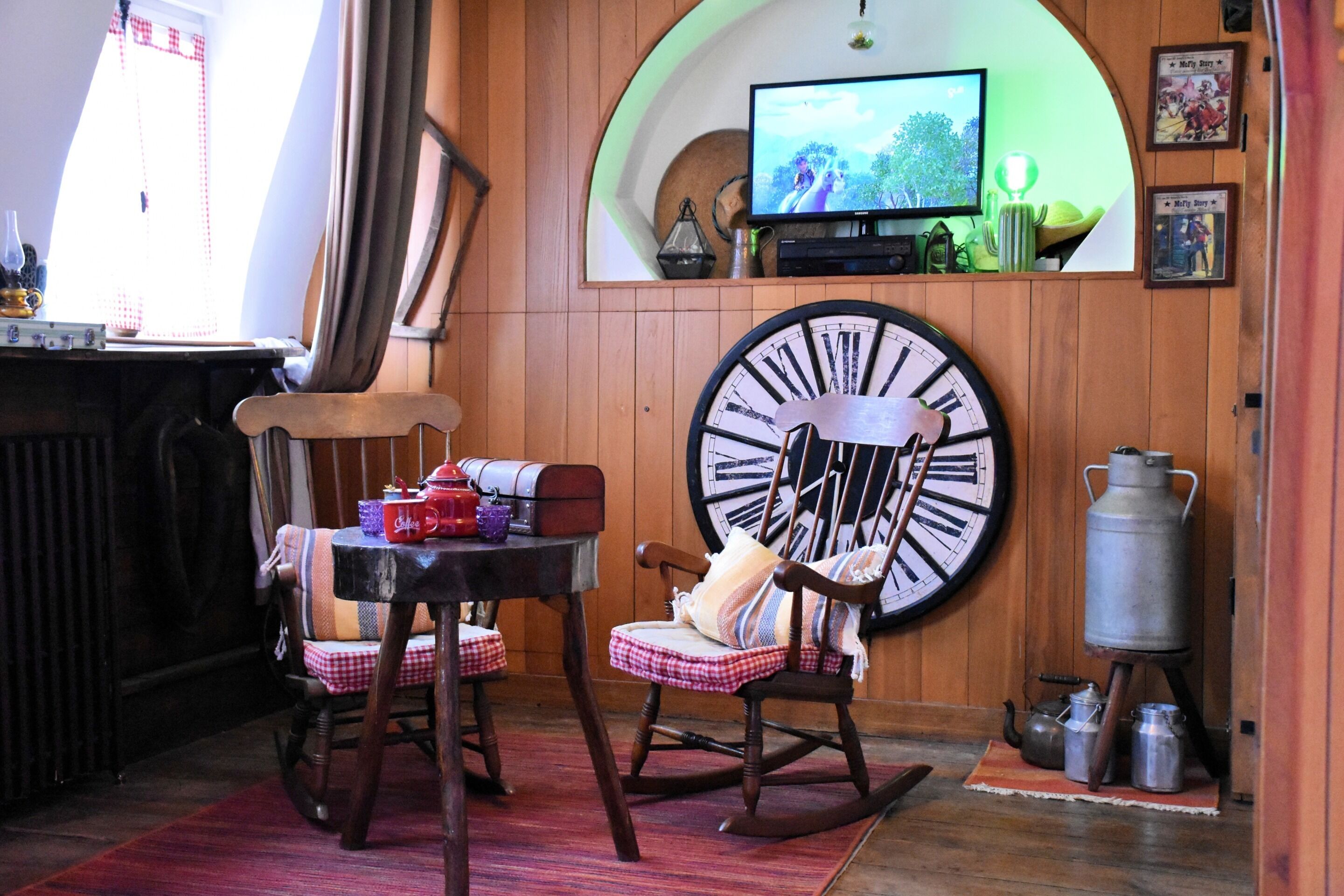 A cozy room with a wooden rocking chair, a large wall clock, and a television mounted on a curved wooden panel.