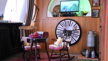A cozy room with a wooden rocking chair, a large wall clock, and a television mounted on a curved wooden panel.
