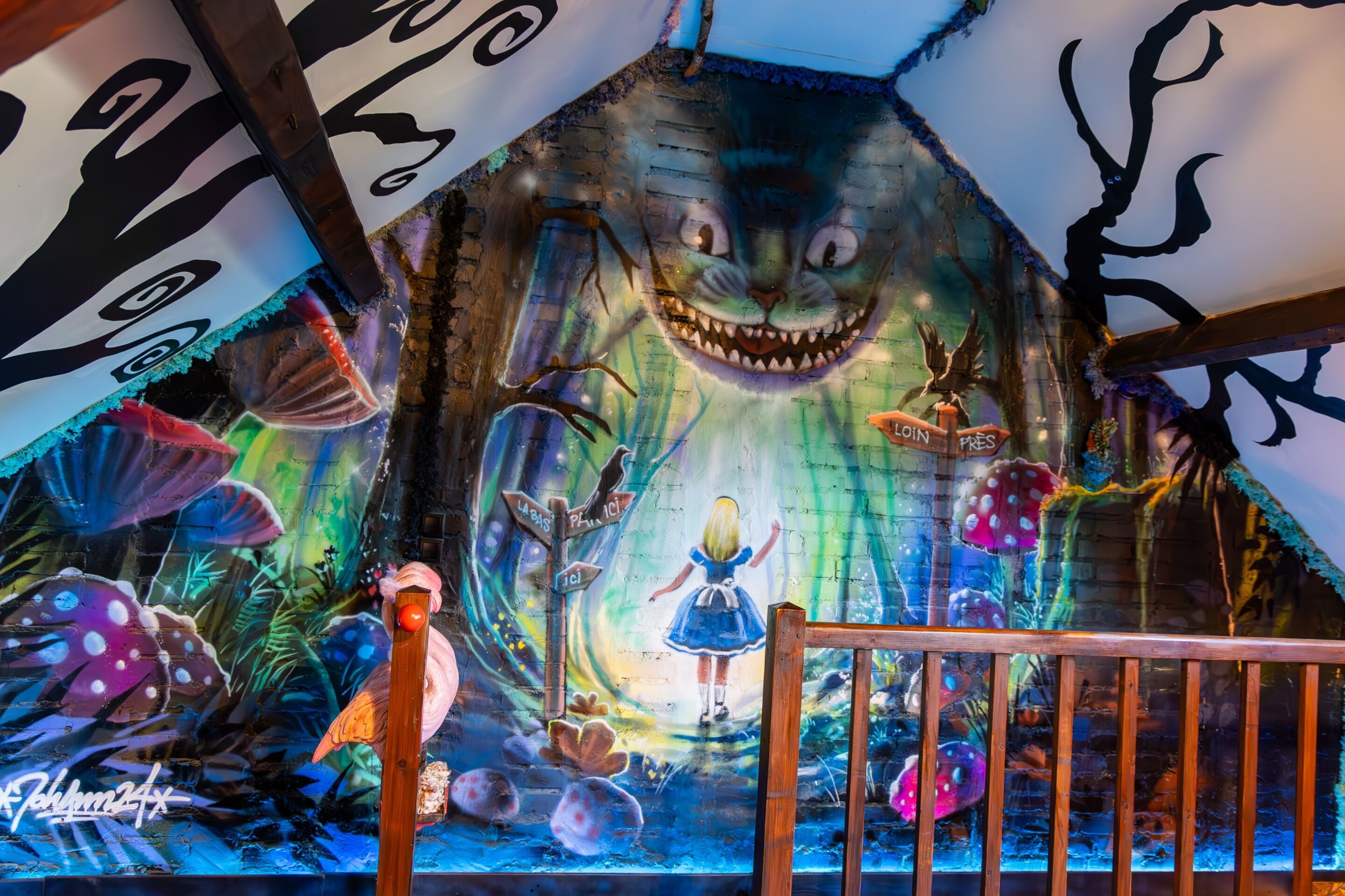 A mural with a large Cheshire Cat and a girl in a blue dress.