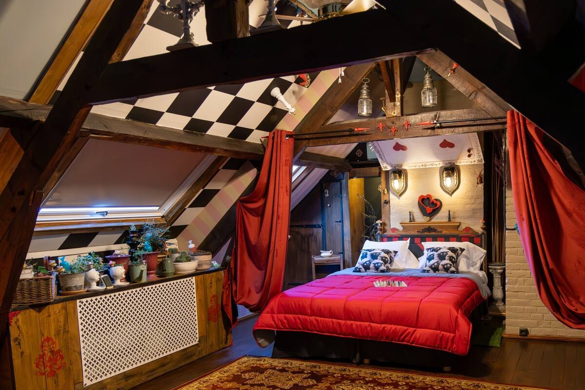 Un dormitorio acogedor en el ático, con colcha roja, vigas de madera y techo a cuadros.