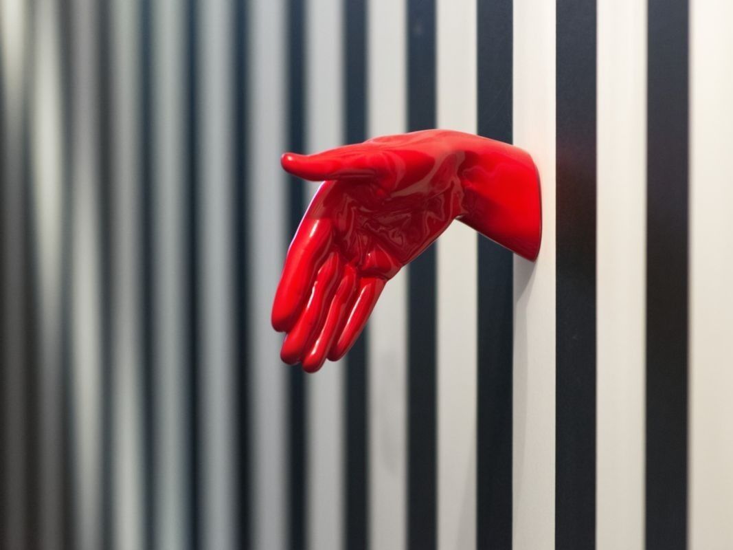 A red hand sculpture against a striped wall.