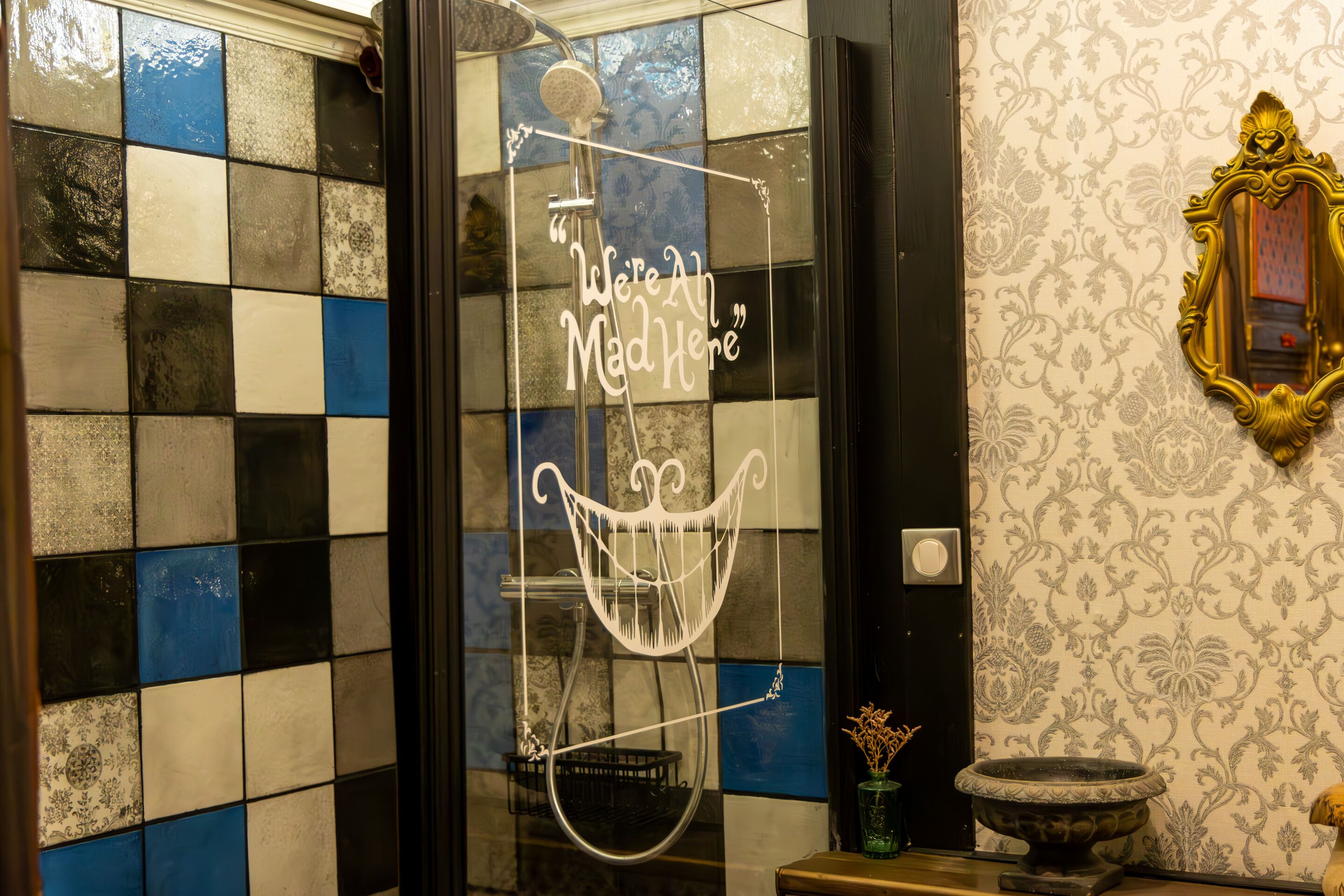 A bathroom with a checkered tile wall, a decorative mirror, and a quote on the glass door.