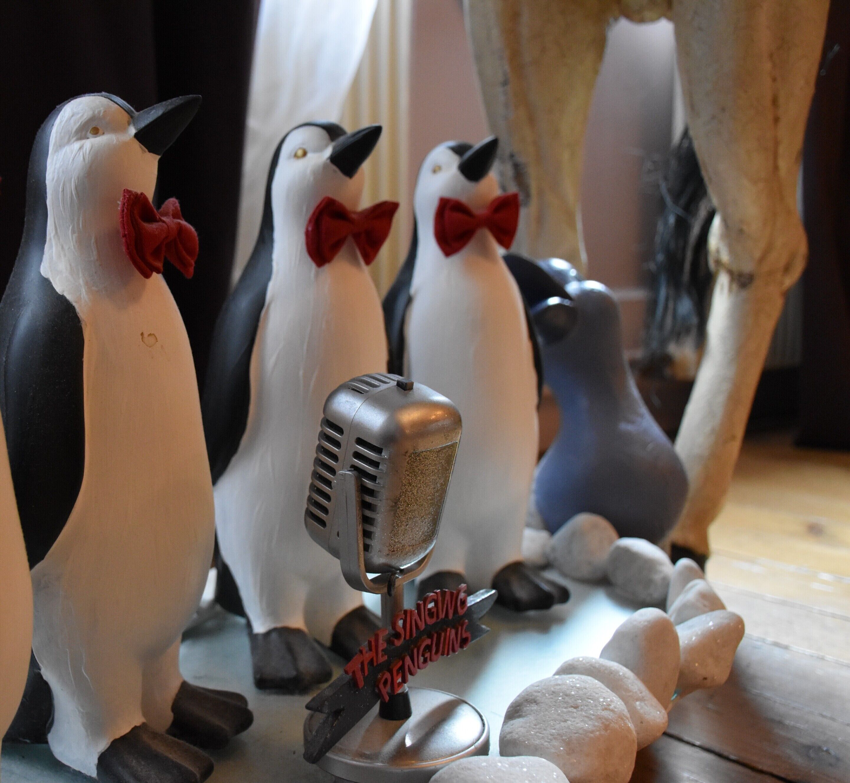 Koristeellisia pingviinihahmoja, joilla on mikrofoni, ja yhdessä niistä on kyltti, jossa lukee: ”Uudet pingviinit”.