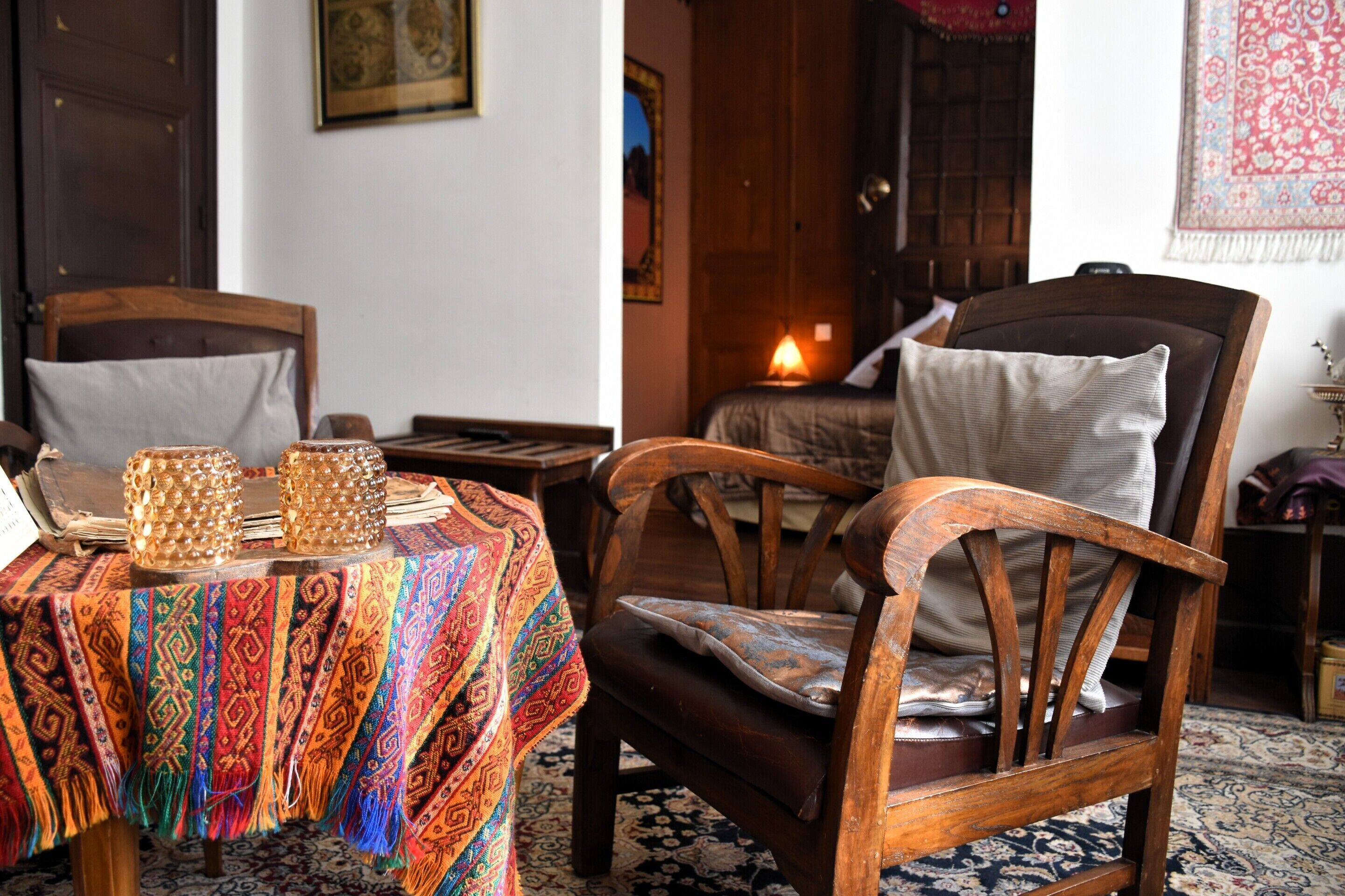 A traditional room with a wooden chair, a table with a patterned tablecloth, and a bed with a white pillow.