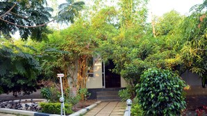 A well-maintained garden with a pathway leading to a building entrance, surrounded by lush greenery and a sign indicating a restaurant. - Wild Wadi Cottages Resort (Mendarda)