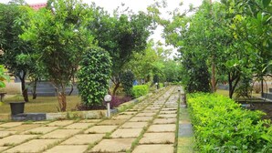 A stone pathway flanked by lush greenery and trees, leading to a building with a red roof. - Wild Wadi Cottages Resort (Mendarda)
