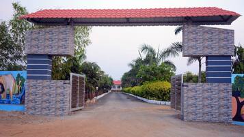 A gated entrance with a red-tiled roof, stone pillars, and a road leading to a building.