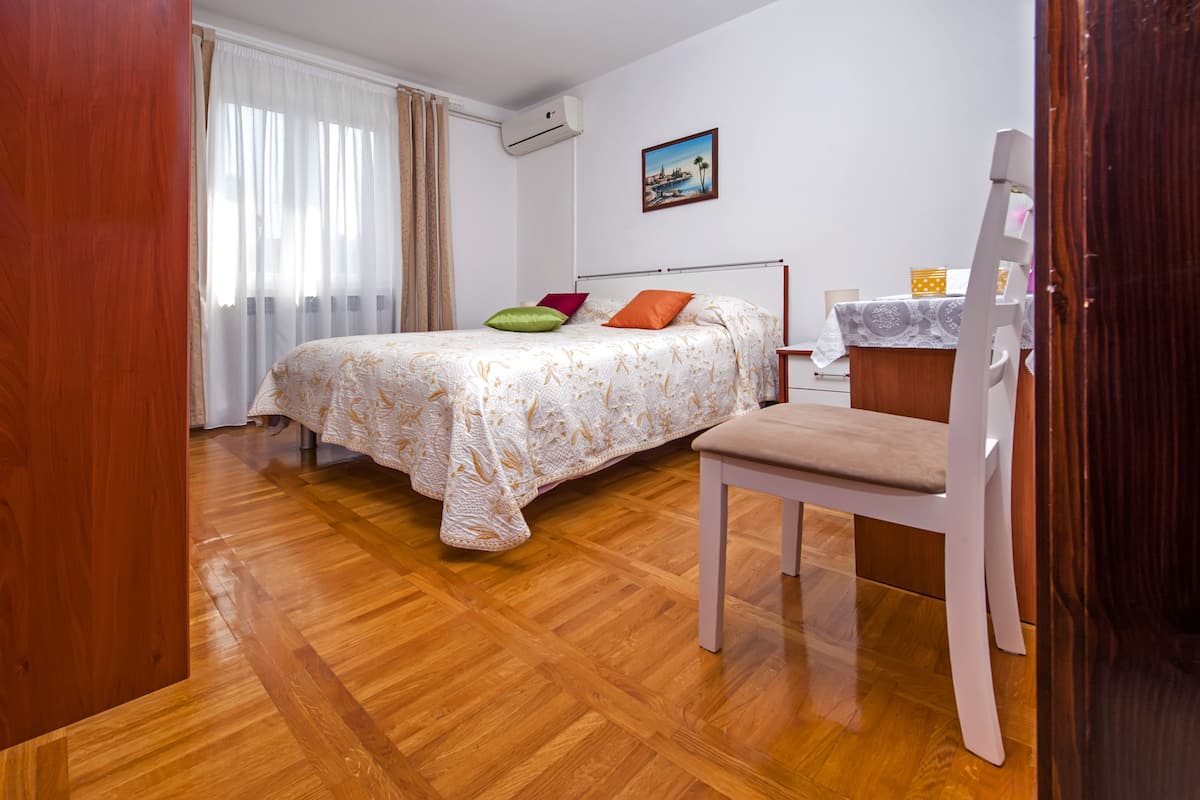 Un dormitorio con una cama, una silla, una mesita de noche y un cuadro en la pared.