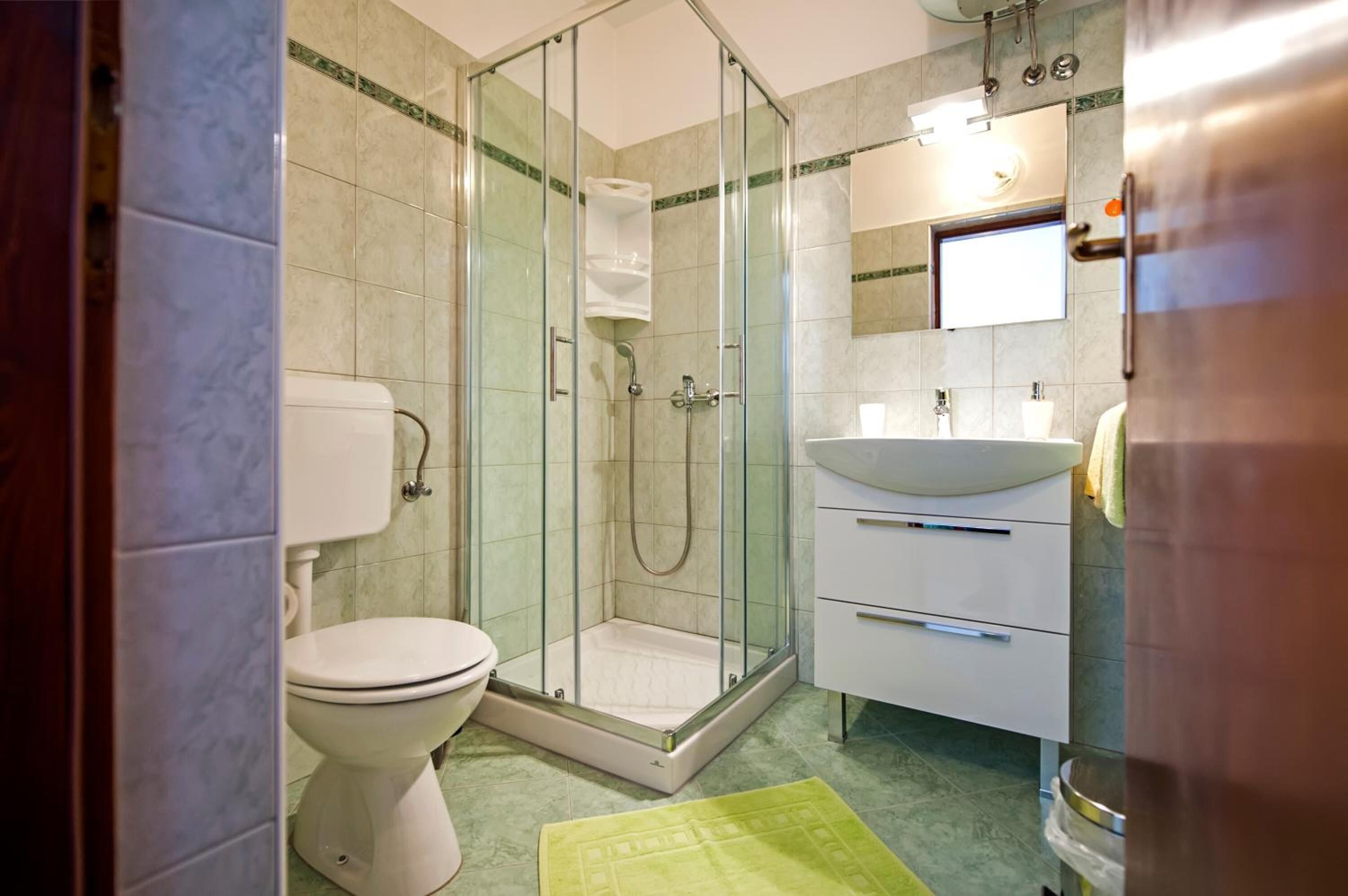 Een badkamer met een douchecabine van glas, een toilet en een wastafel met spiegel.