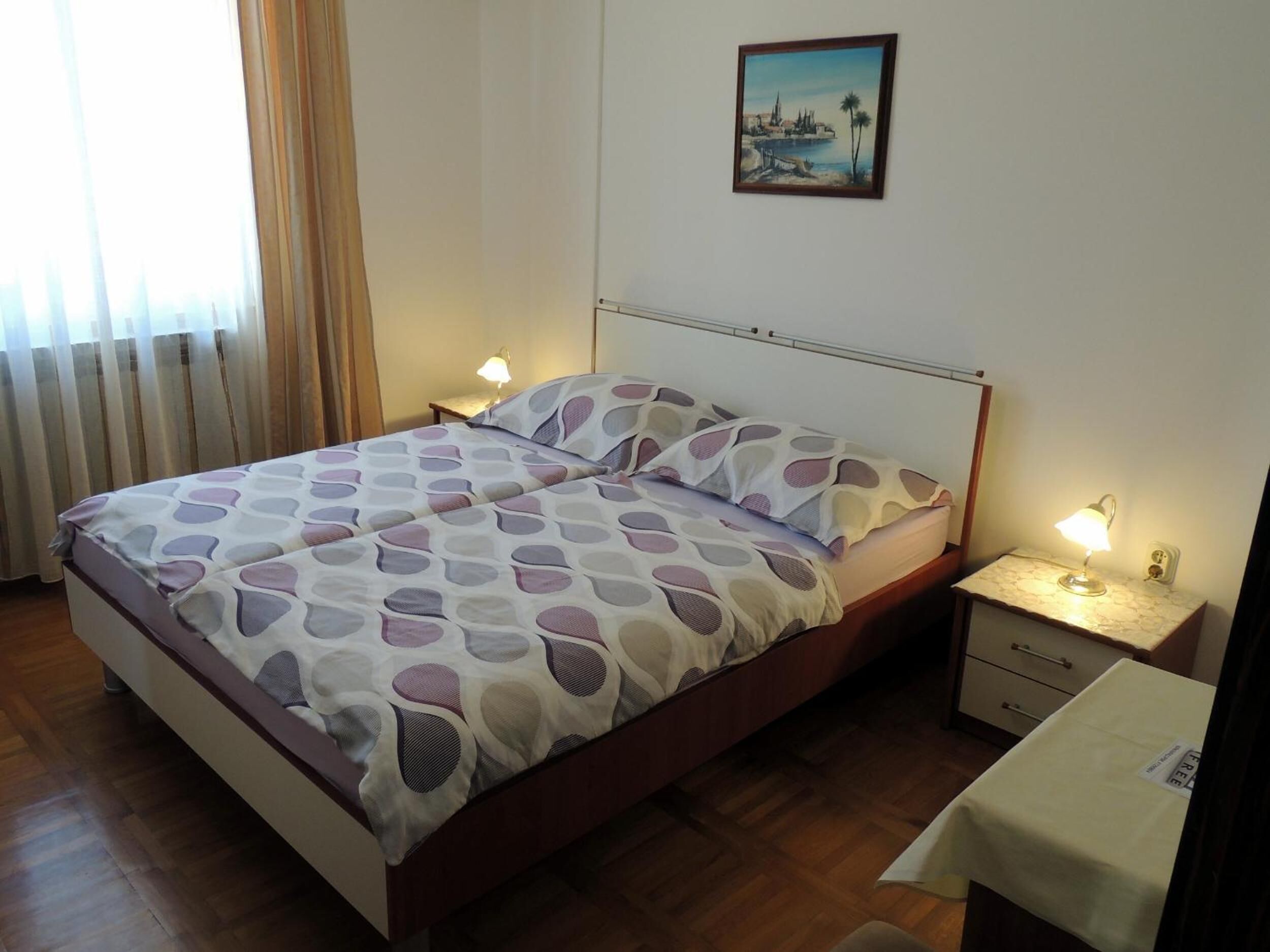 Una cama bien hecha con una colcha estampada, una mesita de noche con una lámpara y un cuadro enmarcado en la pared.