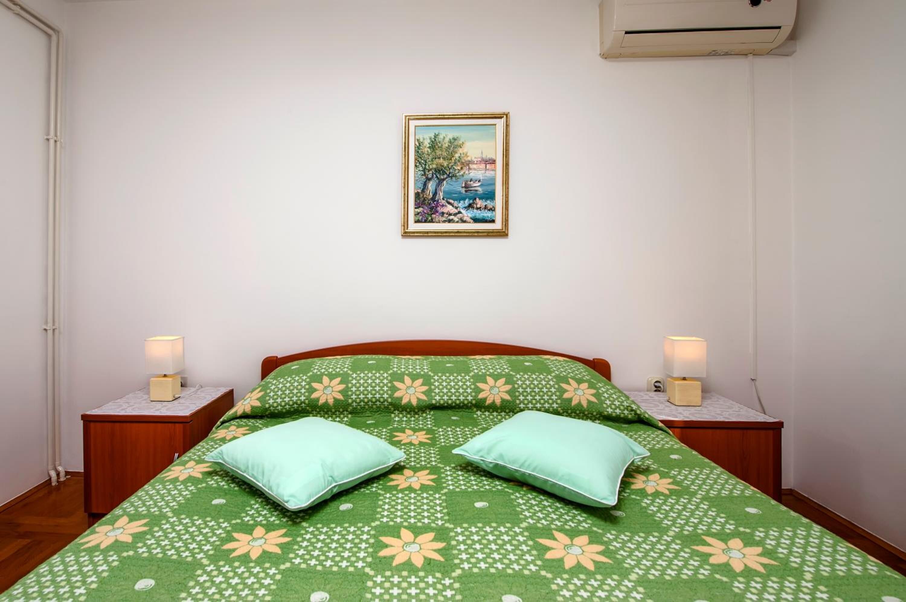 Une chambre à coucher comprenant un lit, deux tables de chevet, une commode, un climatiseur fixé au mur et un tableau encadré accroché au mur.