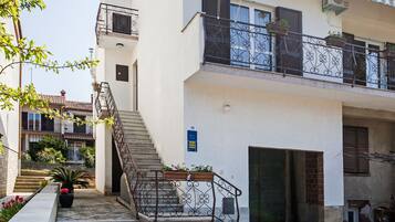 A two-story building with a staircase leading to the entrance, a balcony with metal railings, and a tiled patio area.