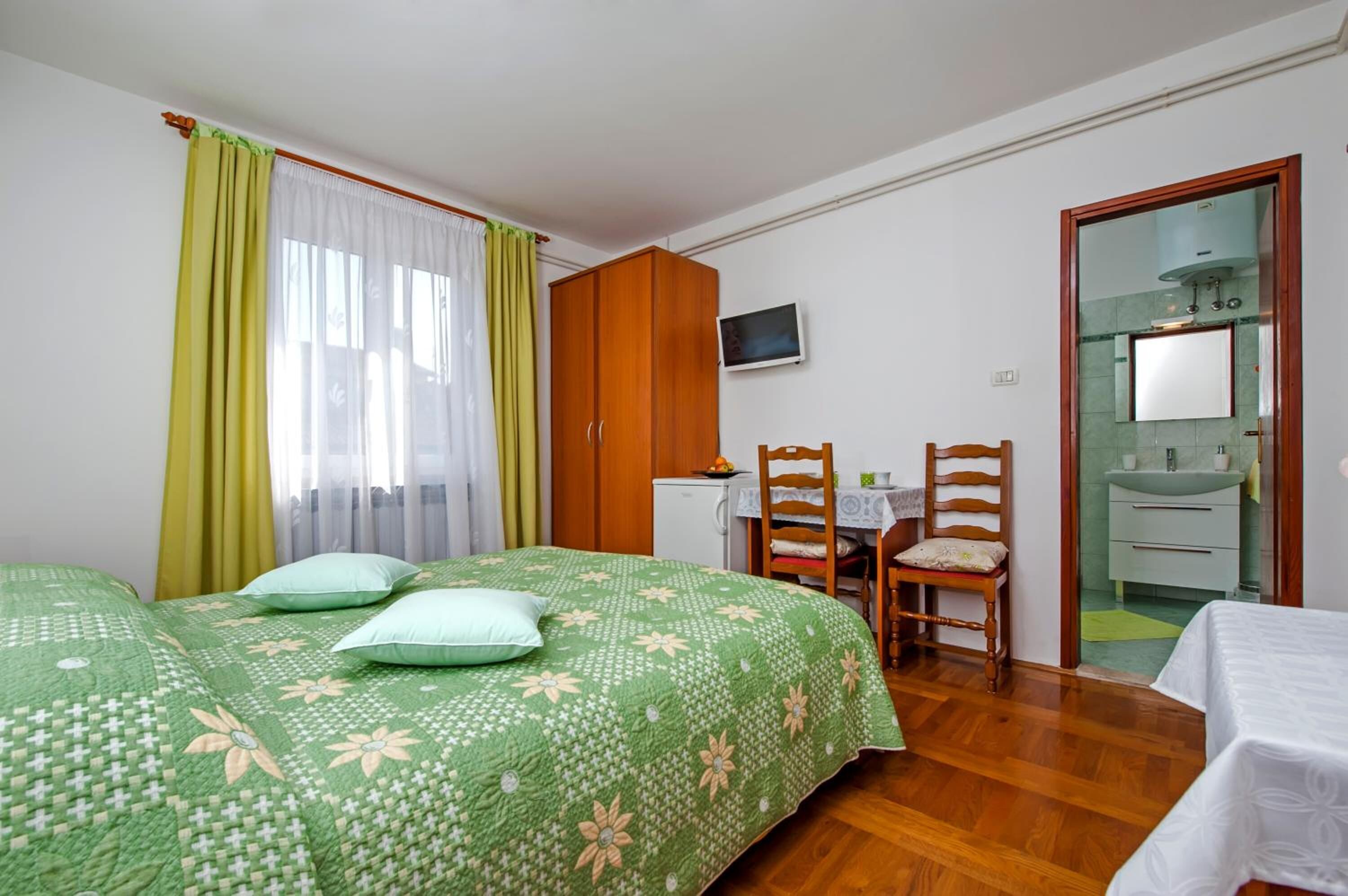 Une chambre à coucher comprenant un lit, deux chaises, un bureau, une télévision et une salle de bain visible à travers une porte ouverte.