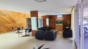 A modern reception area with a wooden wall, seating, a fish tank, and a view of the street. - Hotel Sudoeste (Goiania)