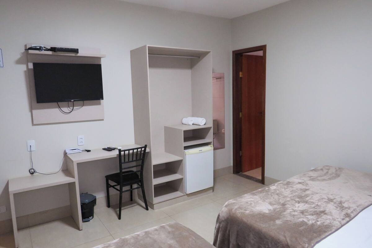 A bedroom with a bed, a desk, a chair, a TV, and a wardrobe.