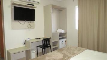 Habitació d'hotel amb llit, escriptori, cadira, televisió, aire condicionat, armari i finestra amb cortines.