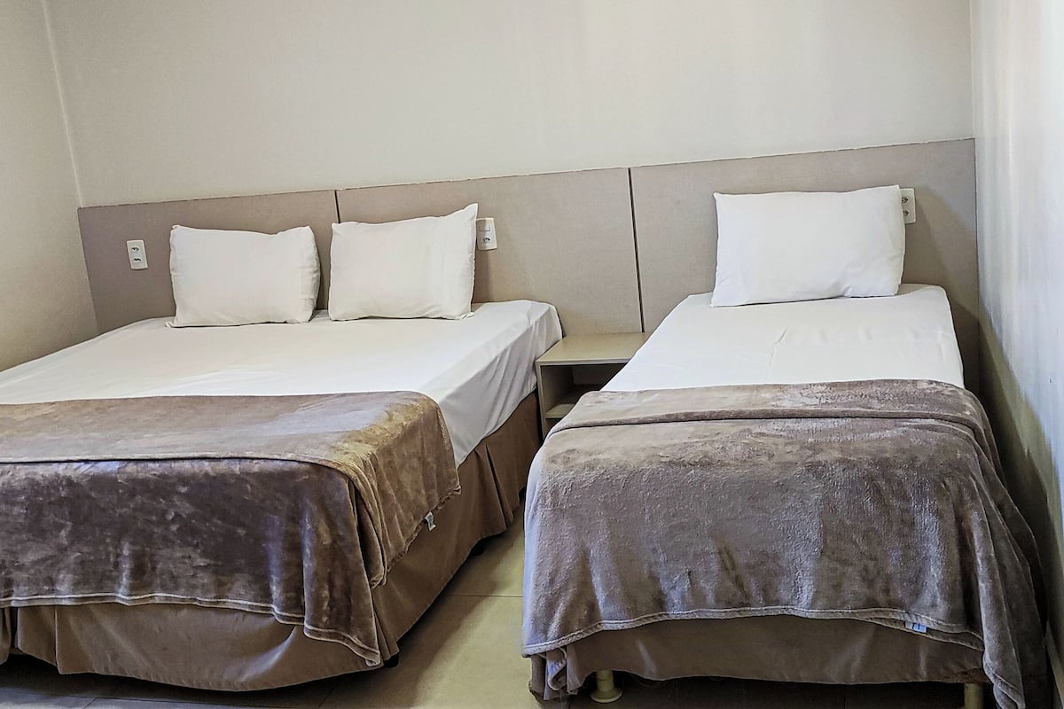 A hotel room with two single beds, each with a headboard and pillows, and a brown bedspread.