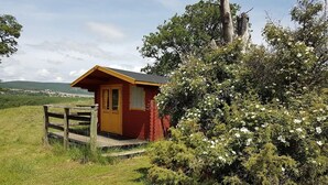 A small wooden cabin with a red exterior, surrounded by lush greenery and a clear sky. - LES TRUFFIERS Cabane (Limans)