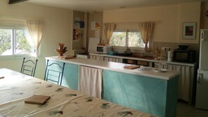 A compact kitchen with a central island, a dining table, and a window with curtains. - LES TRUFFIERS Cabane (Limans)