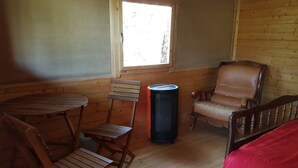 A wooden interior with a round table, two chairs, a red bed, and a window. - LES TRUFFIERS Cabane (Limans)