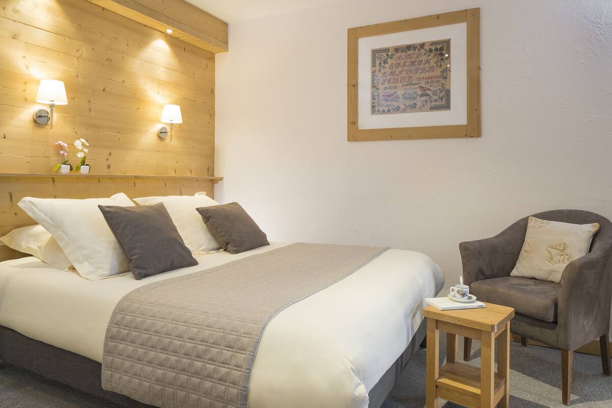 A neatly made bed with a quilted blanket, two bedside lamps, a framed artwork on the wall, and a small wooden table with a cup and saucer.