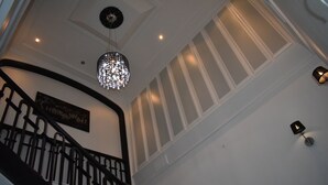 A staircase with a black railing, a chandelier, and a wall-mounted light fixture. - Le Trianon de Salies (Salies-de-Bearn)