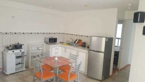 A compact kitchen with white cabinets, a stainless steel refrigerator, a microwave, and a dining table with orange chairs. - Coriñawi Apartment for Rent (Cusco)