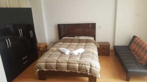 A bedroom with a bed, a sofa, a TV, and a dresser. - Coriñawi Apartment for Rent (Cusco)