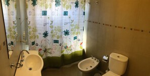 A bathroom with a sink, bidet, toilet, and a shower curtain with floral patterns. - La Cascada Duplex (San Martín de los Andes)