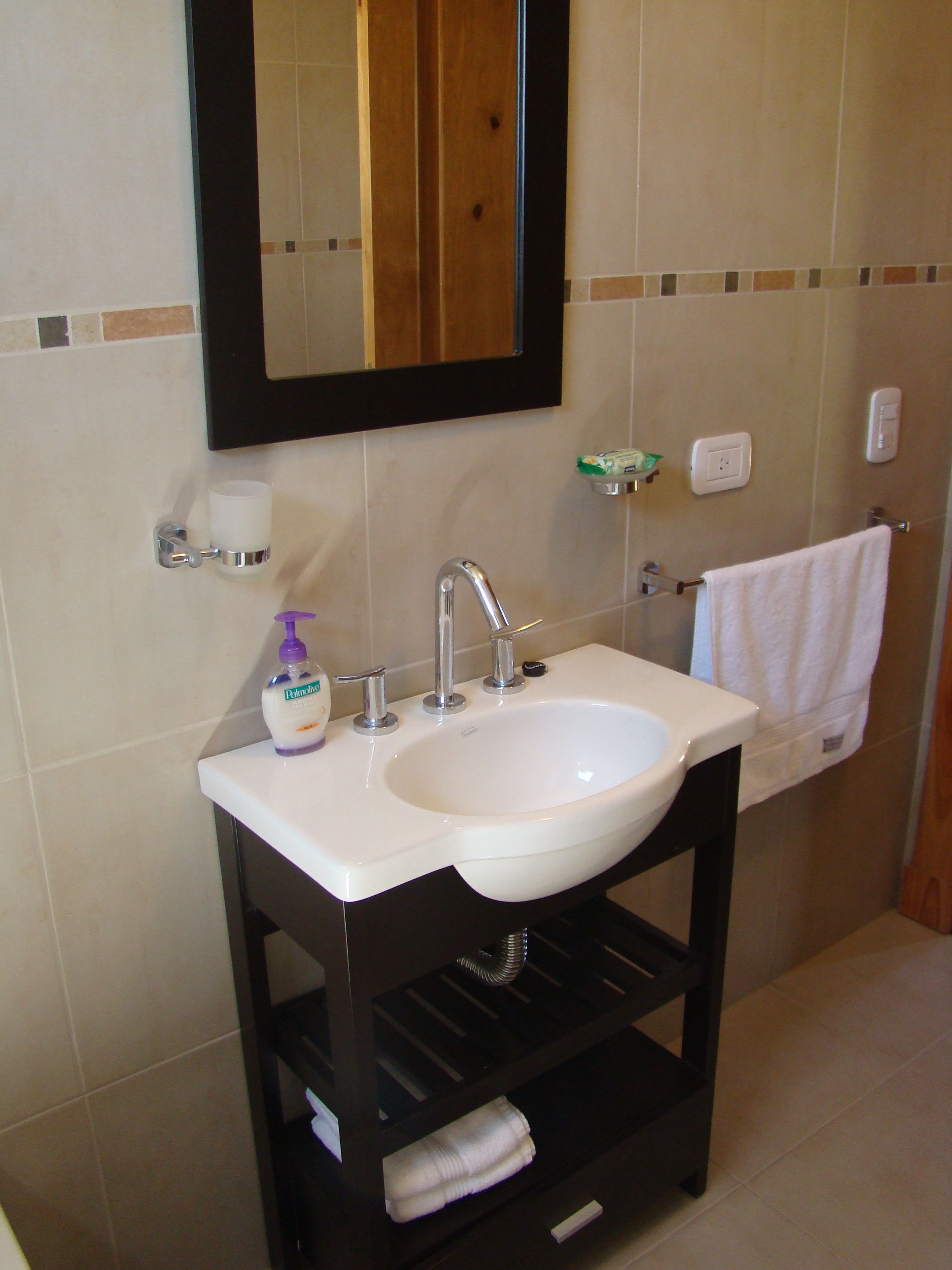 Un baño con lavamanos blanco, un espejo, toallero y dispensador de jabón.