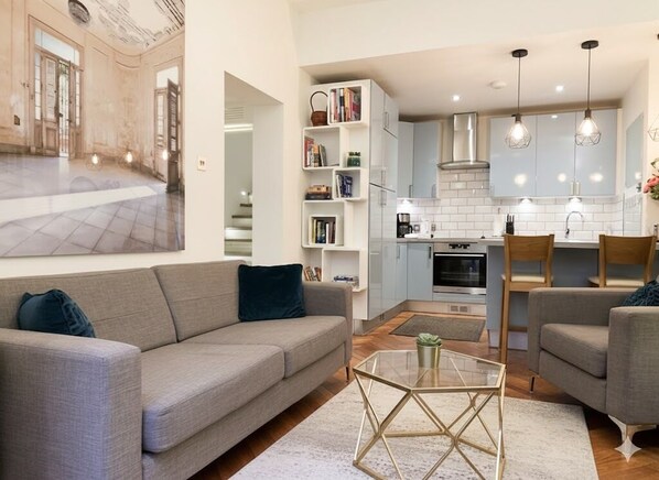 A modern living room with a grey sofa, a glass coffee table, and a bookshelf.