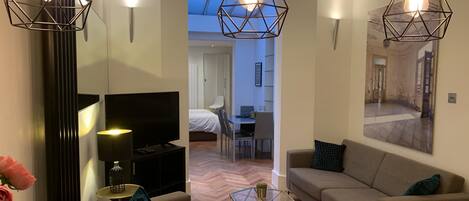 Una sala de estar moderna con sofá, mesa de centro, televisor e iluminación decorativa.