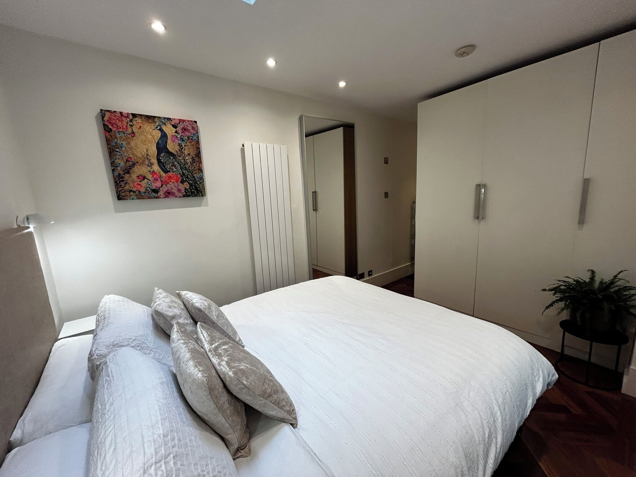 A bedroom with a bed, a radiator, a door, and a potted plant.