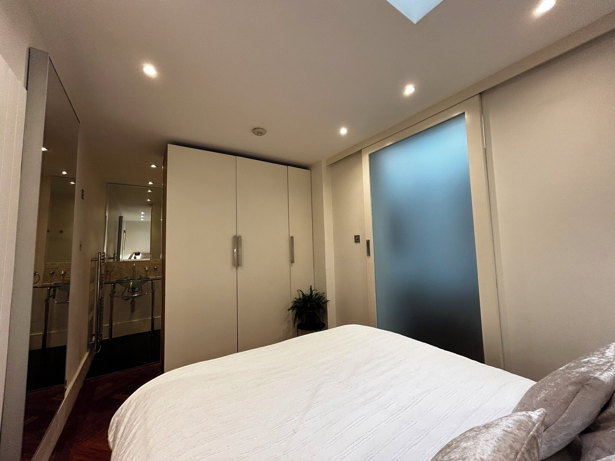Ein Schlafzimmer mit Bett, Schrank, Spiegel und einer kleinen Pflanze.