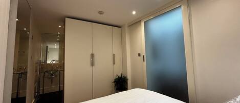 Ein Schlafzimmer mit Bett, Schrank, Spiegel und einer kleinen Pflanze.