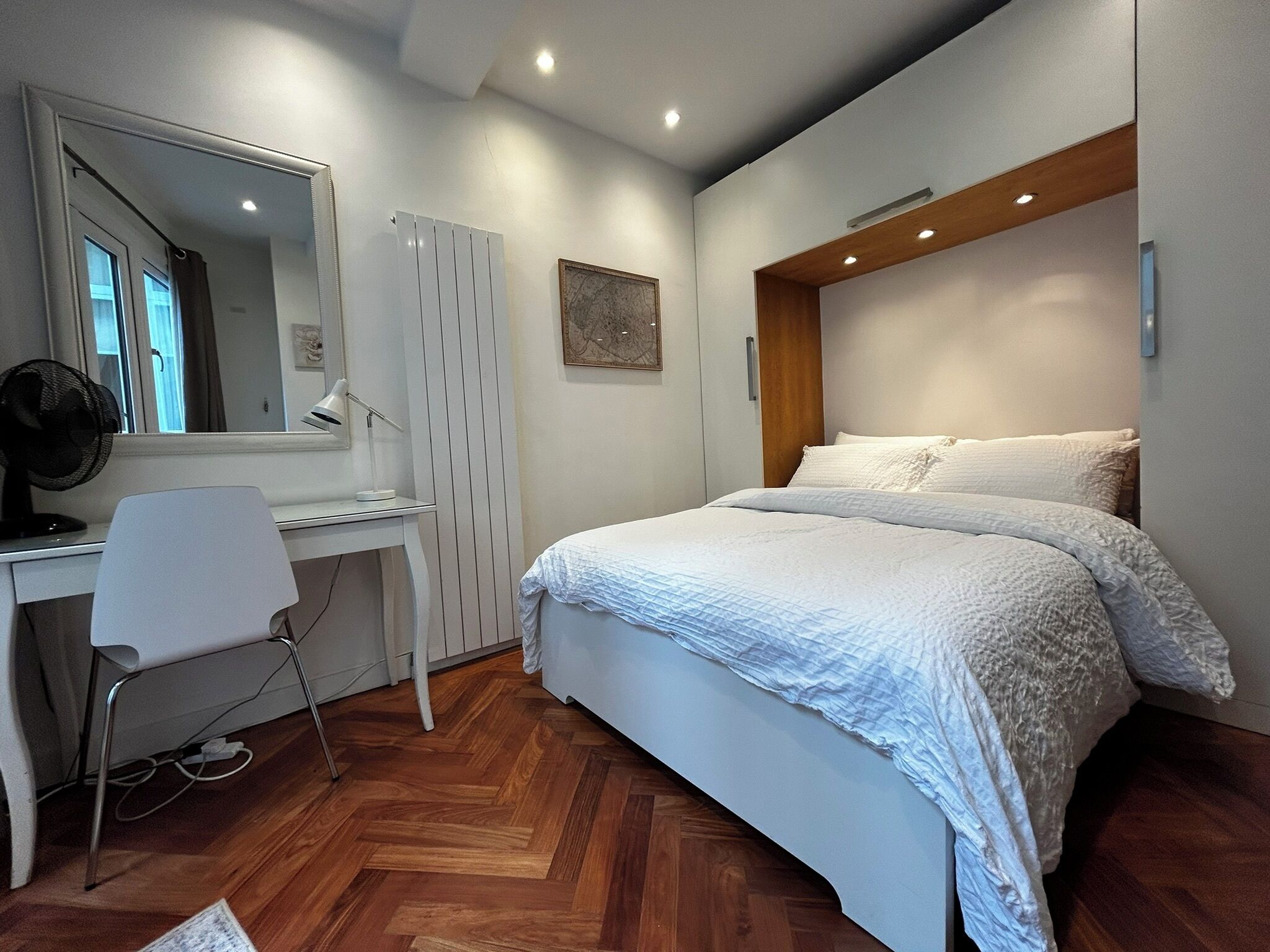 A bedroom with a bed, a desk, a chair, a mirror, and a radiator.