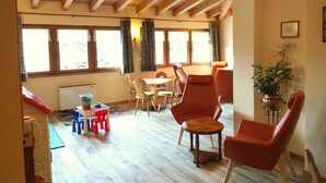 A spacious room with a high wooden ceiling, a dining area with chairs and a table, and large windows with curtains. - Hotel Zurigo (Molveno)