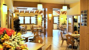 A restaurant with wooden furniture, multiple dining tables, and chairs. There are large windows allowing natural light, and the ceiling has wooden beams. - Hotel Zurigo (Molveno)