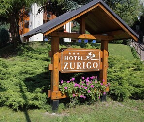 Un letrero de madera del Hotel Zúrich con una pequeña estructura de techo y flores rosas en la base.