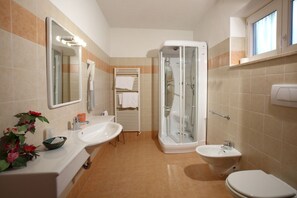 Un baño con lavamanos, bidé, inodoro y ducha con mampara de vidrio.
