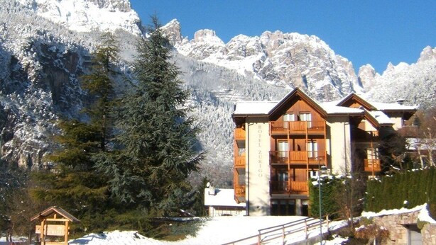 A hotel with multiple wooden balconies, set against a backdrop of snow-covered mountains. - Hotel Zurigo (Molveno)