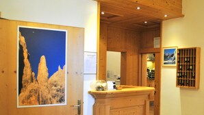 A wooden reception desk with a framed picture of a mountain landscape on the wall to the left. - Hotel Zurigo (Molveno)