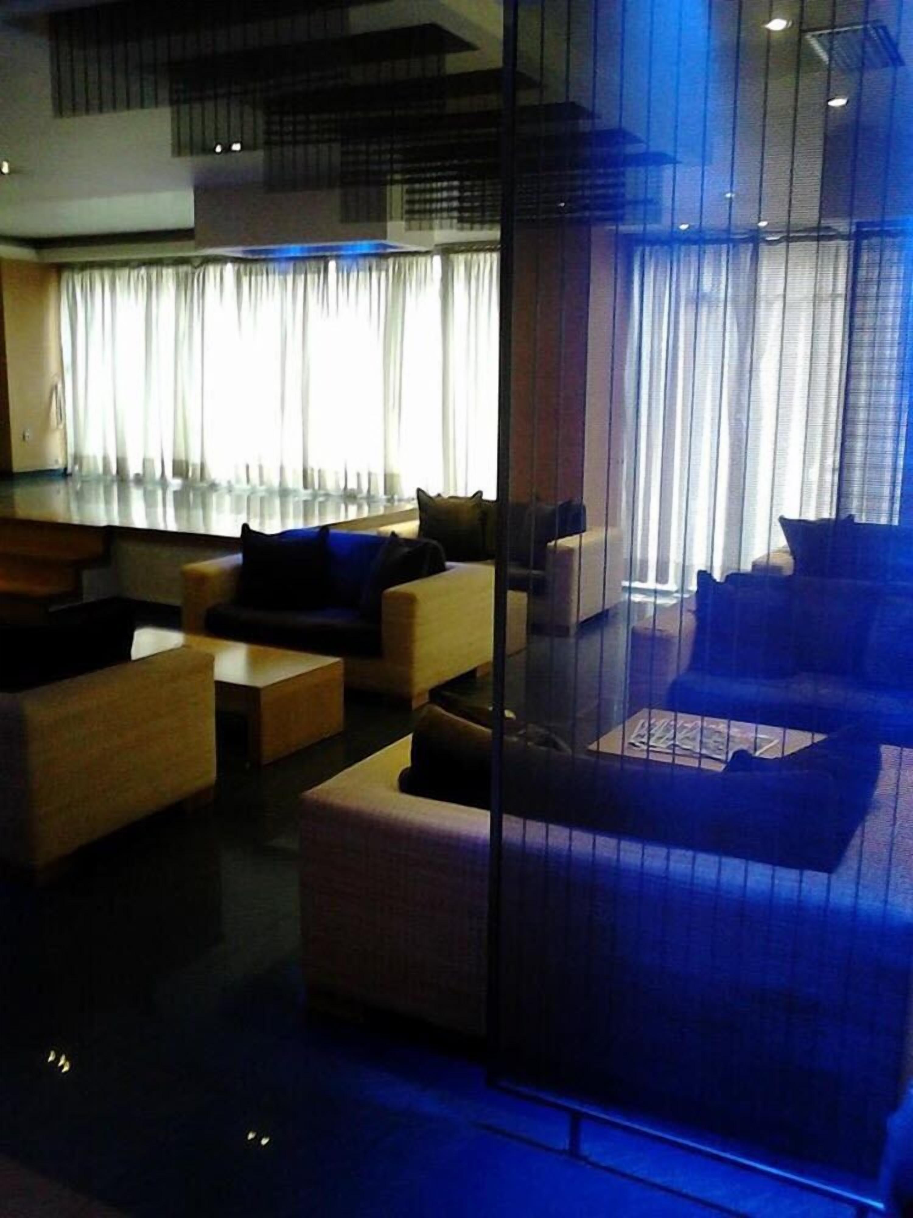 A modern living room with a glass partition, comfortable seating, and a large window with curtains.