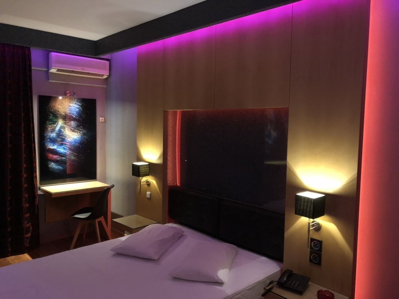 A hotel room with a bed, desk, and two wall-mounted lamps.