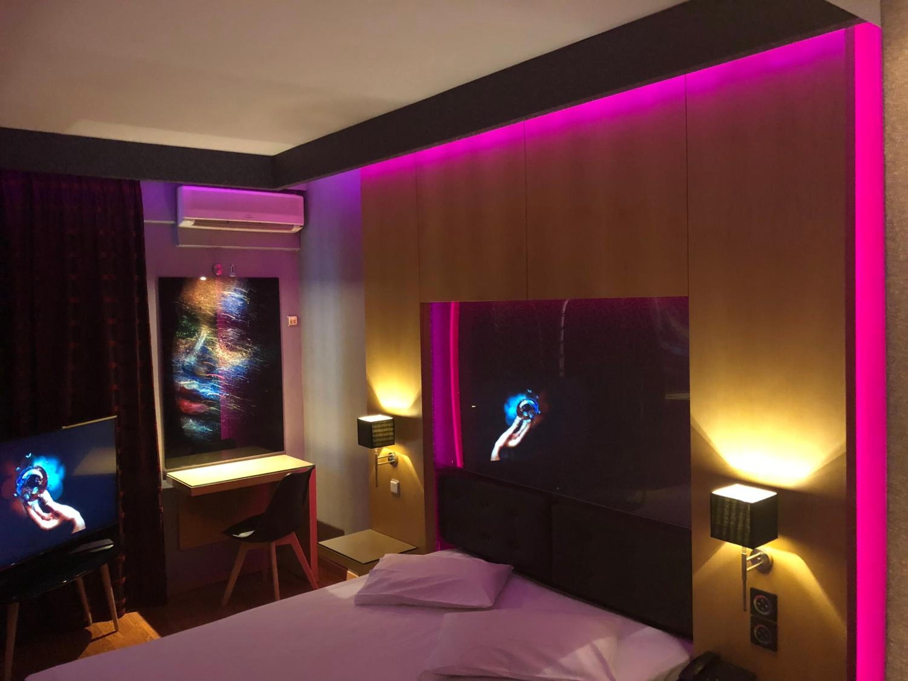 Habitación de hotel con cama, escritorio y dos televisores montados en la pared.