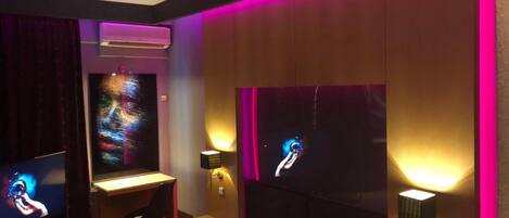 Habitación de hotel con cama, escritorio y dos televisores montados en la pared.