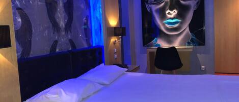 A modern hotel room with a large bed, a wall-mounted TV, and a unique blue-lit artwork on the wall.