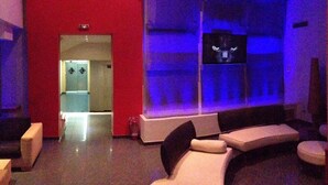A modern lounge area with a red accent wall, a glass partition, and a flat-screen TV mounted on the wall. - Olympic Hotel – Adults Only (Piraeus)