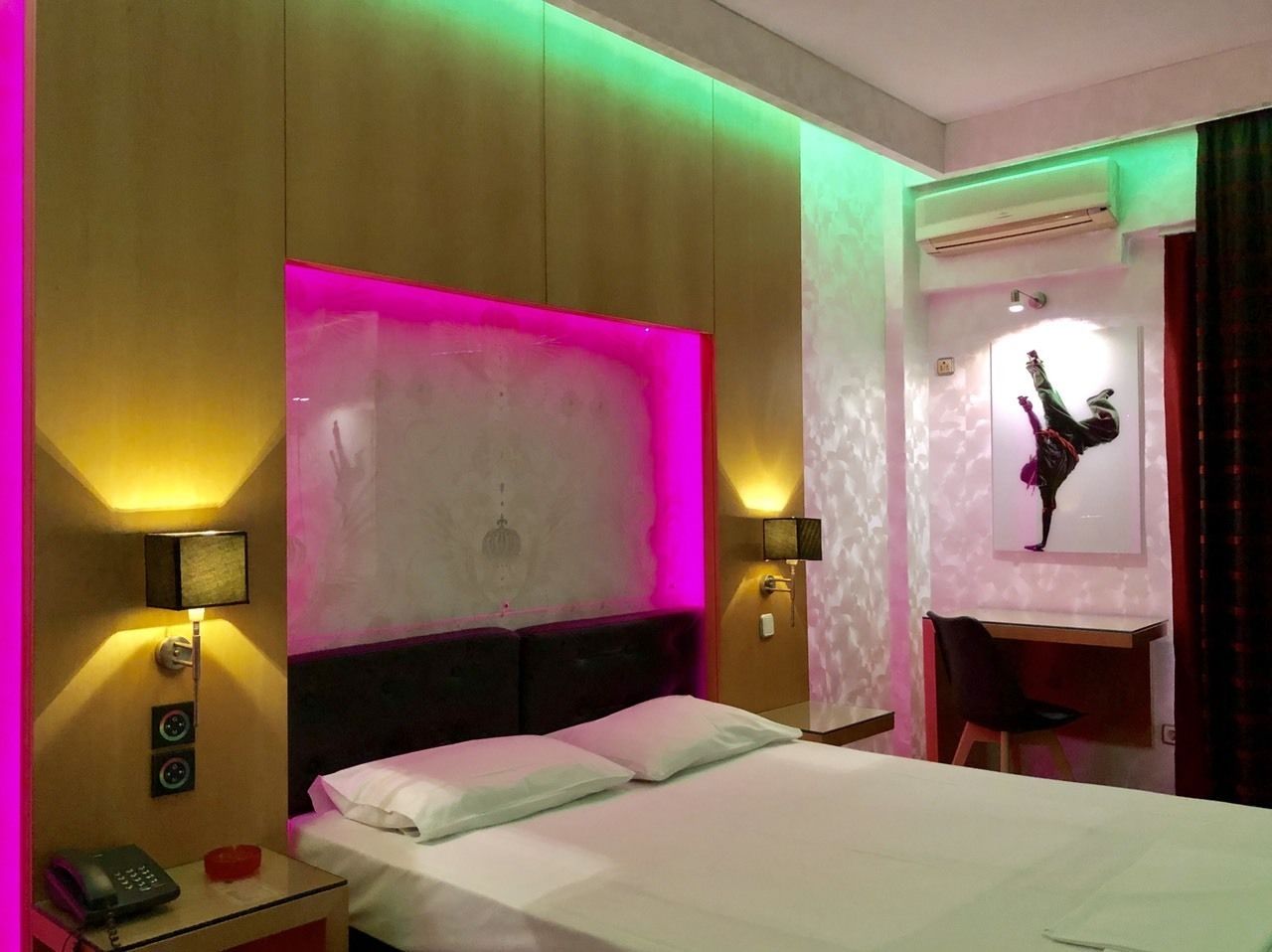 Una habitación de hotel con cama, lámparas de noche, un escritorio y un aire acondicionado de pared.