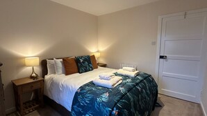 Ein ordentlich bezogenes Bett mit Blumenmusterdecke, zwei Nachttischlampen und ein Nachttisch mit einer Schublade.